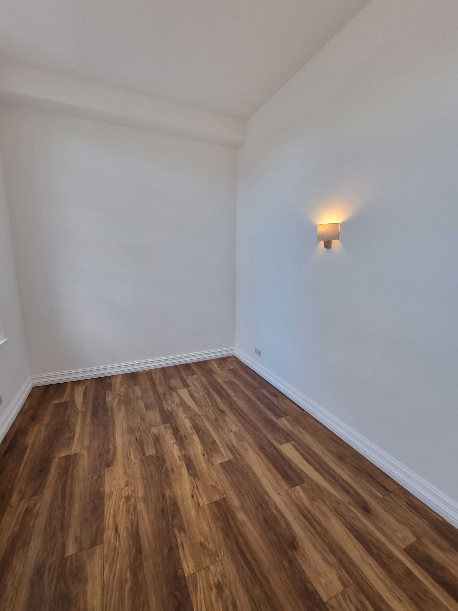Empty room with wood-look floor, white walls, and a wall sconce casting warm light.