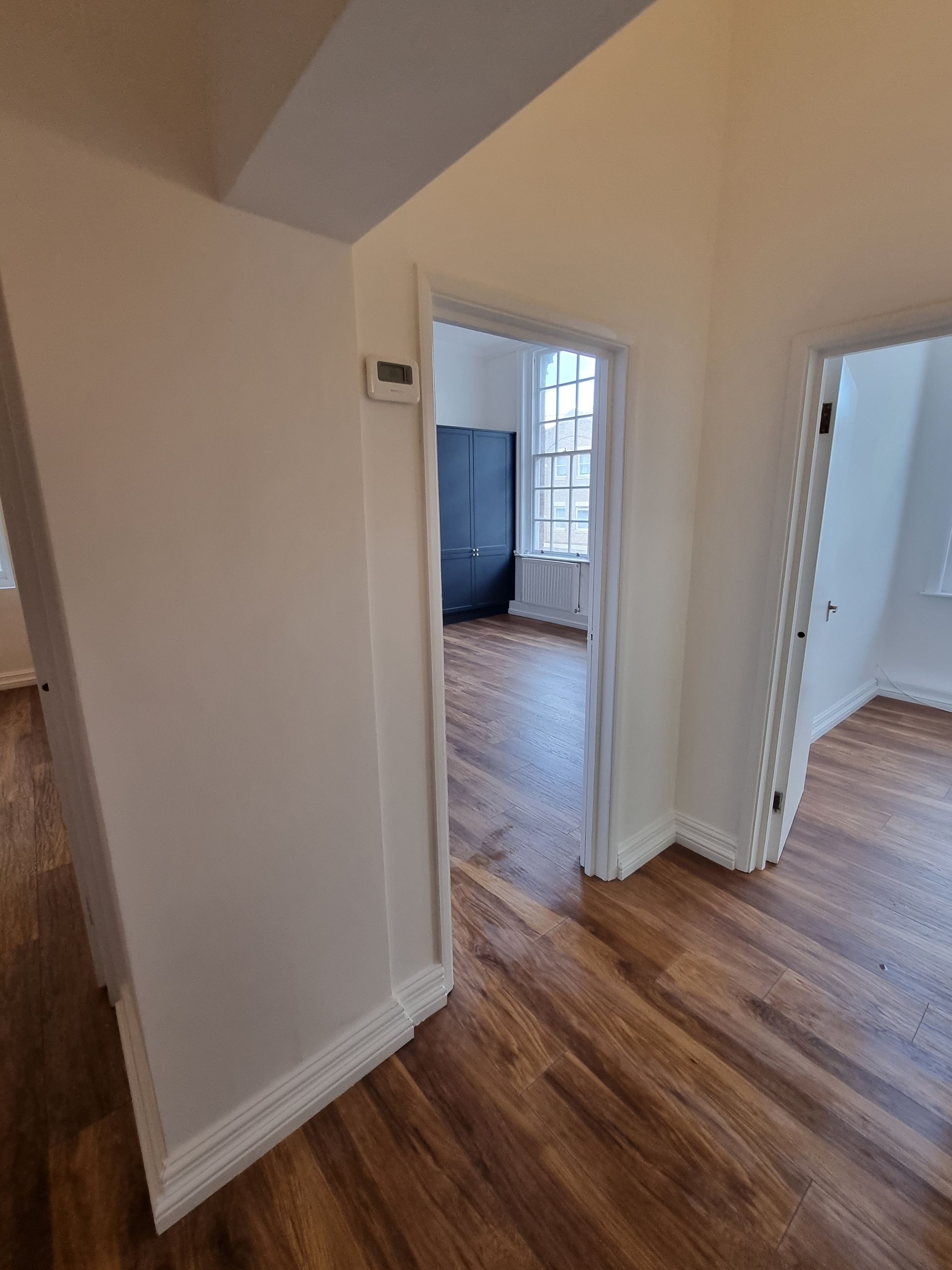 A hallway leading to a living room with hardwood floors and white walls.