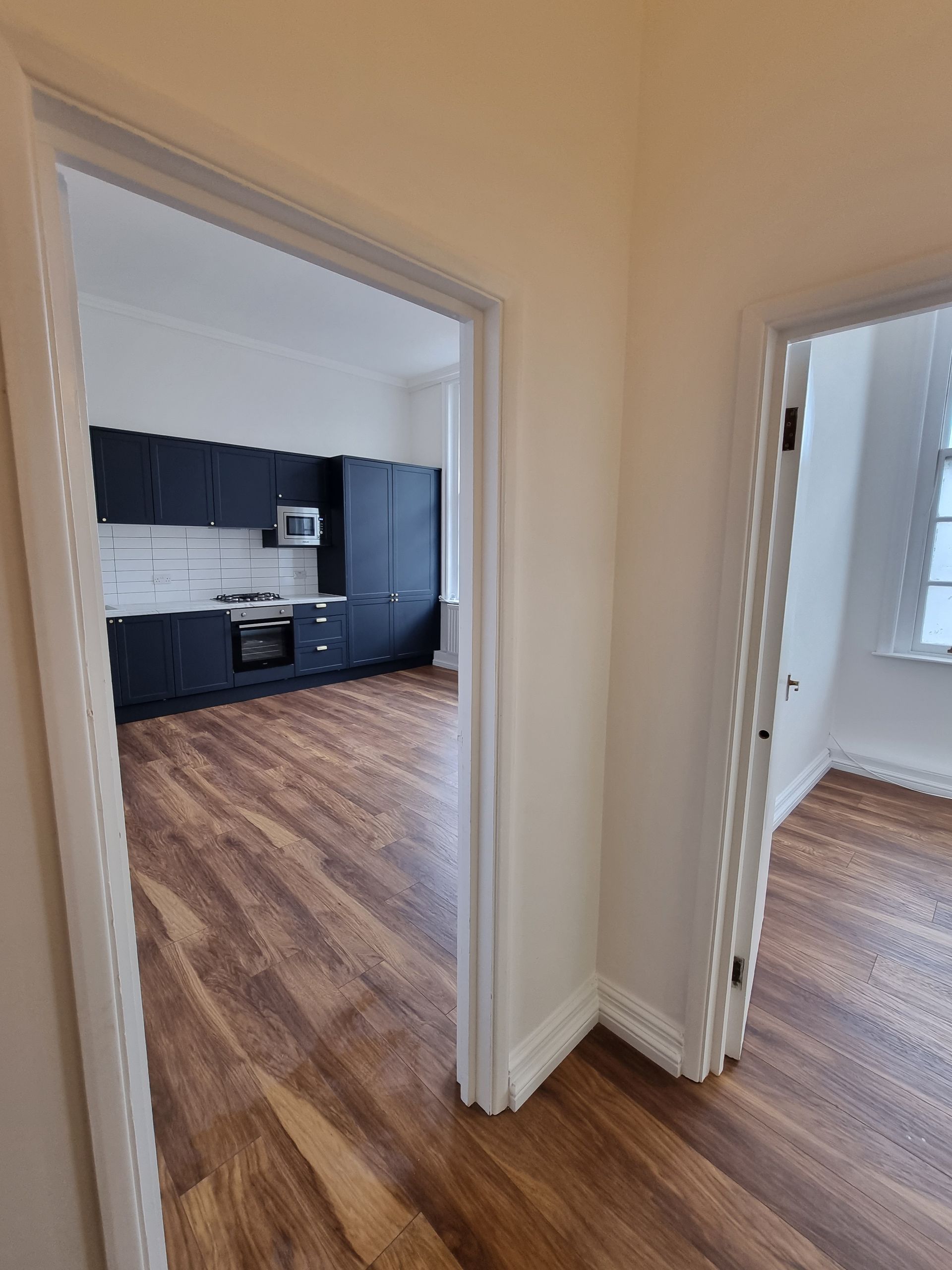 A hallway leading to a kitchen with hardwood floors and black cabinets.