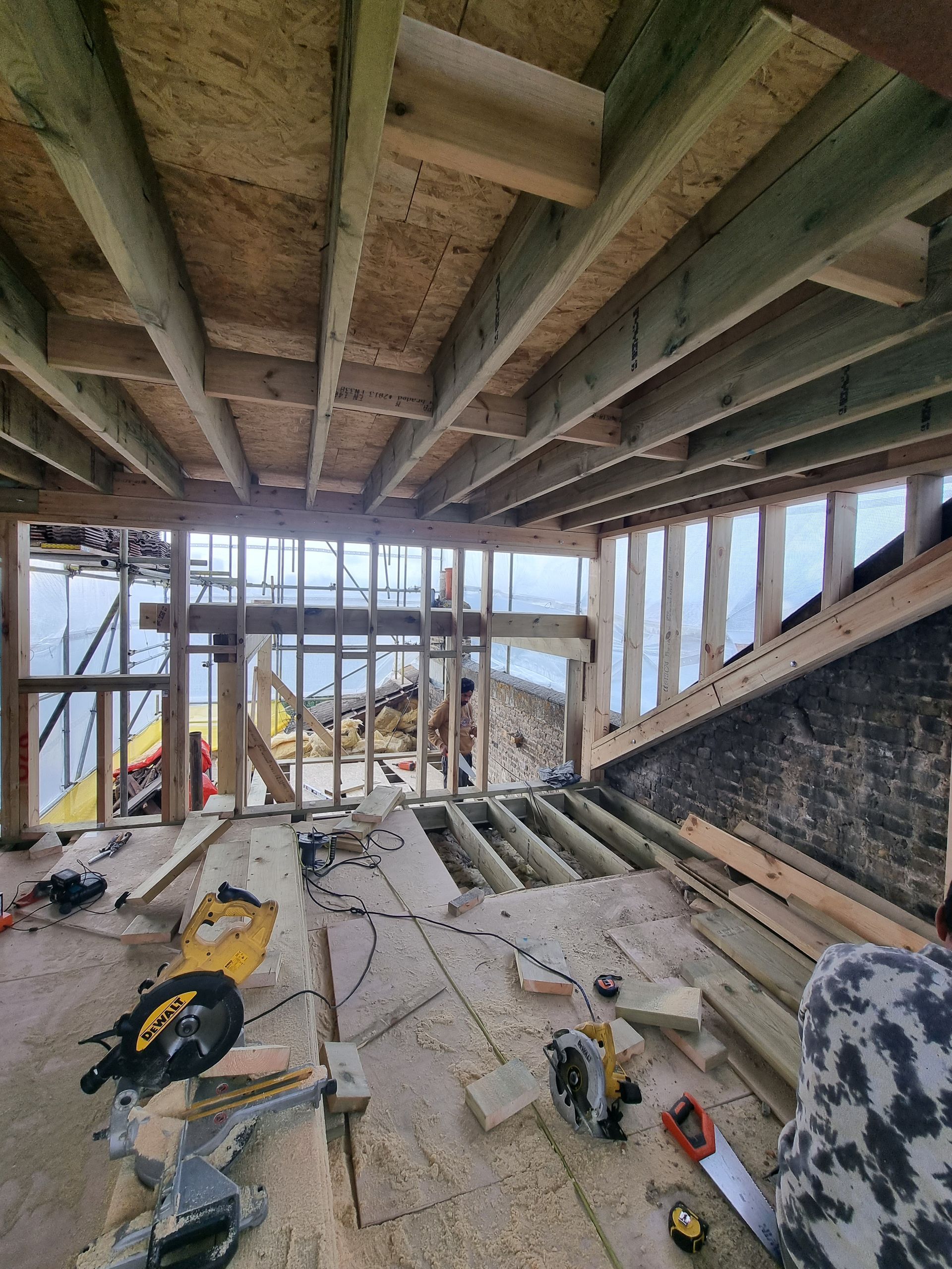 A room with a lot of wooden beams and a circular saw on the floor.