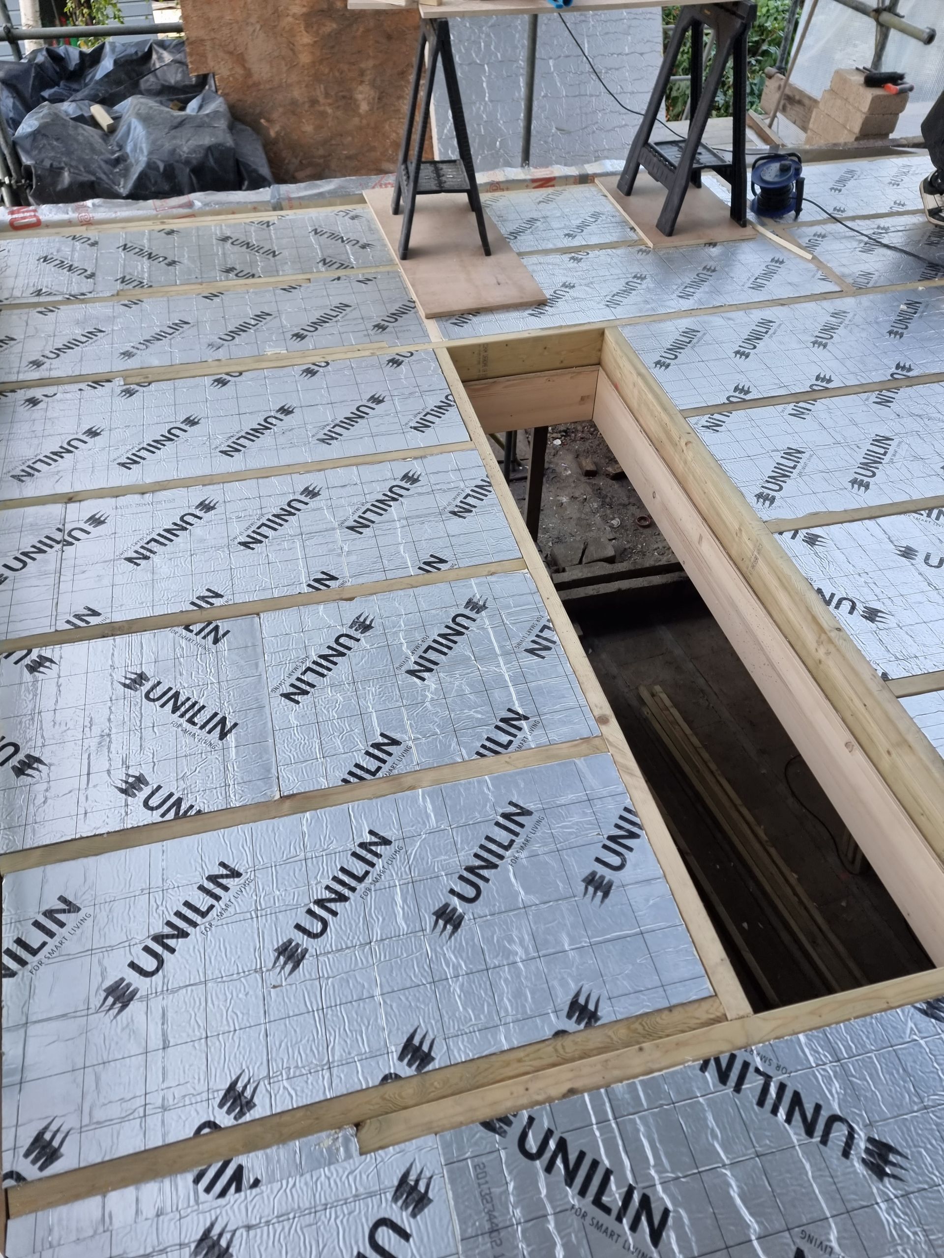 Construction site: Floor insulation with silver panels, wood framing, and an open access point.