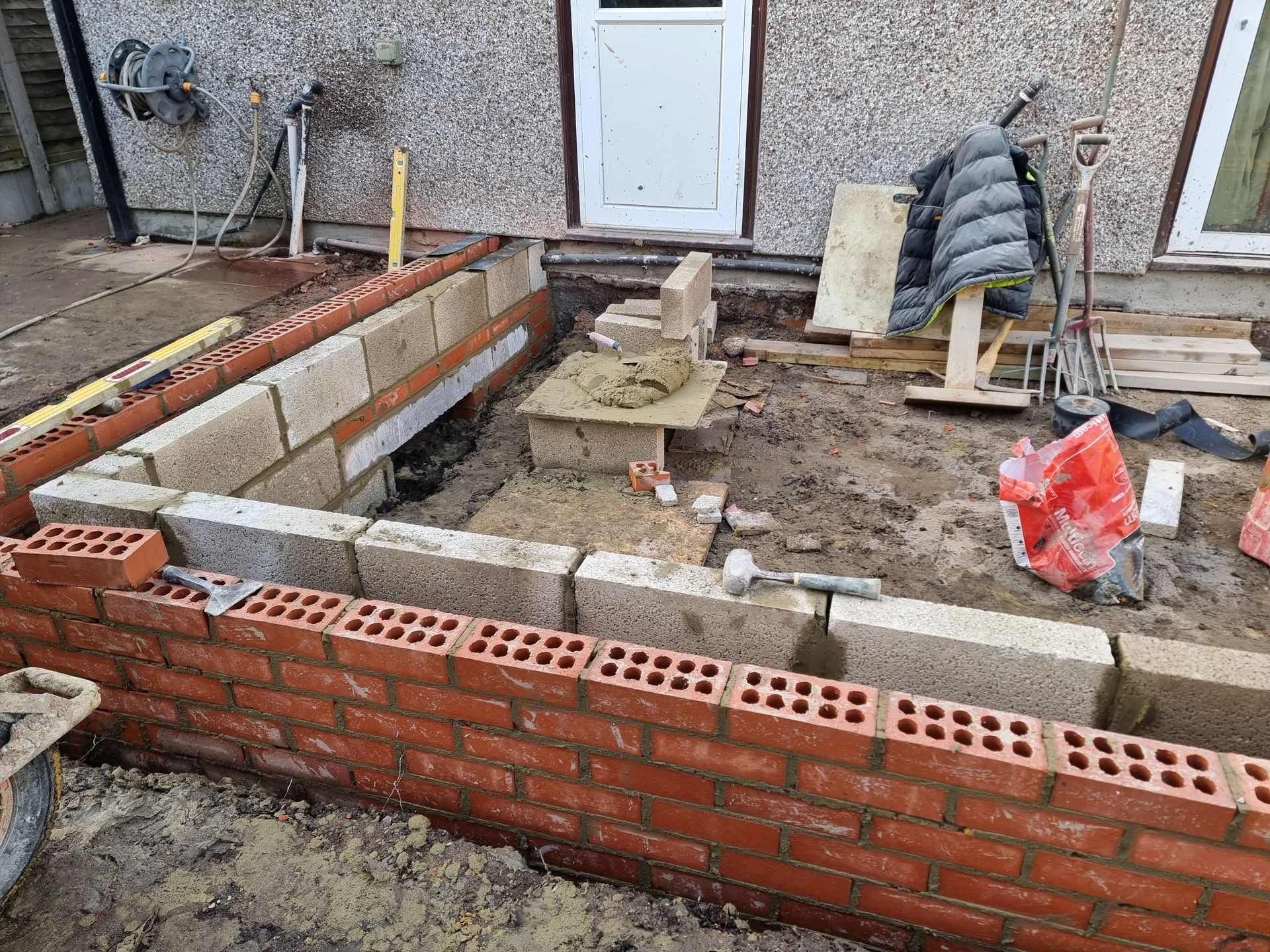 Brick and block construction of an outdoor structure, with tools and materials scattered around.