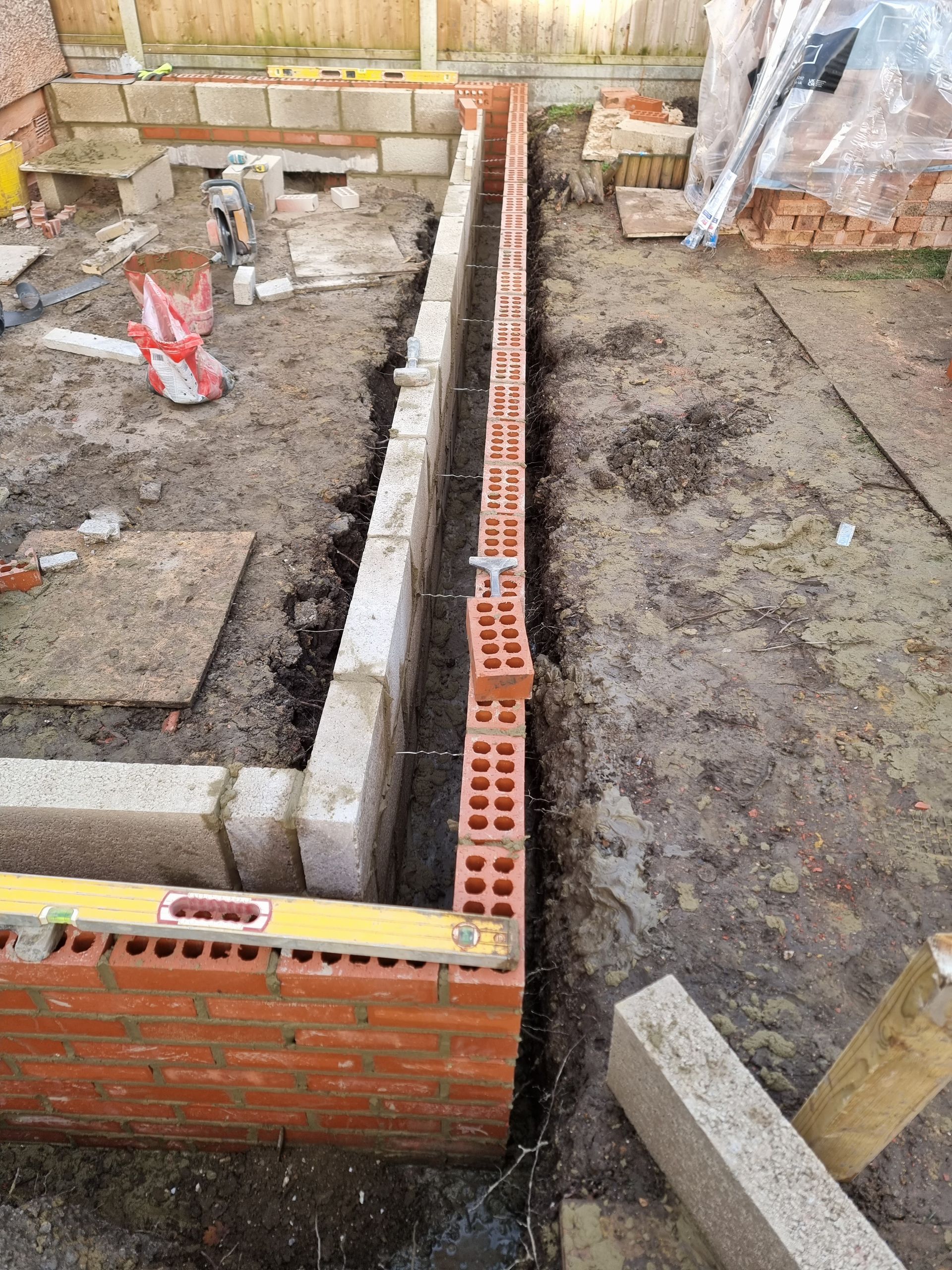 Brick and concrete construction site with a trench, partially built walls, and tools.