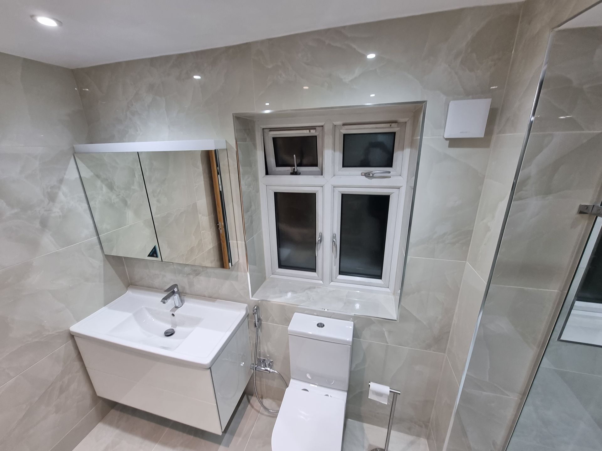 Modern bathroom with a white sink, toilet, window, and tiled walls.