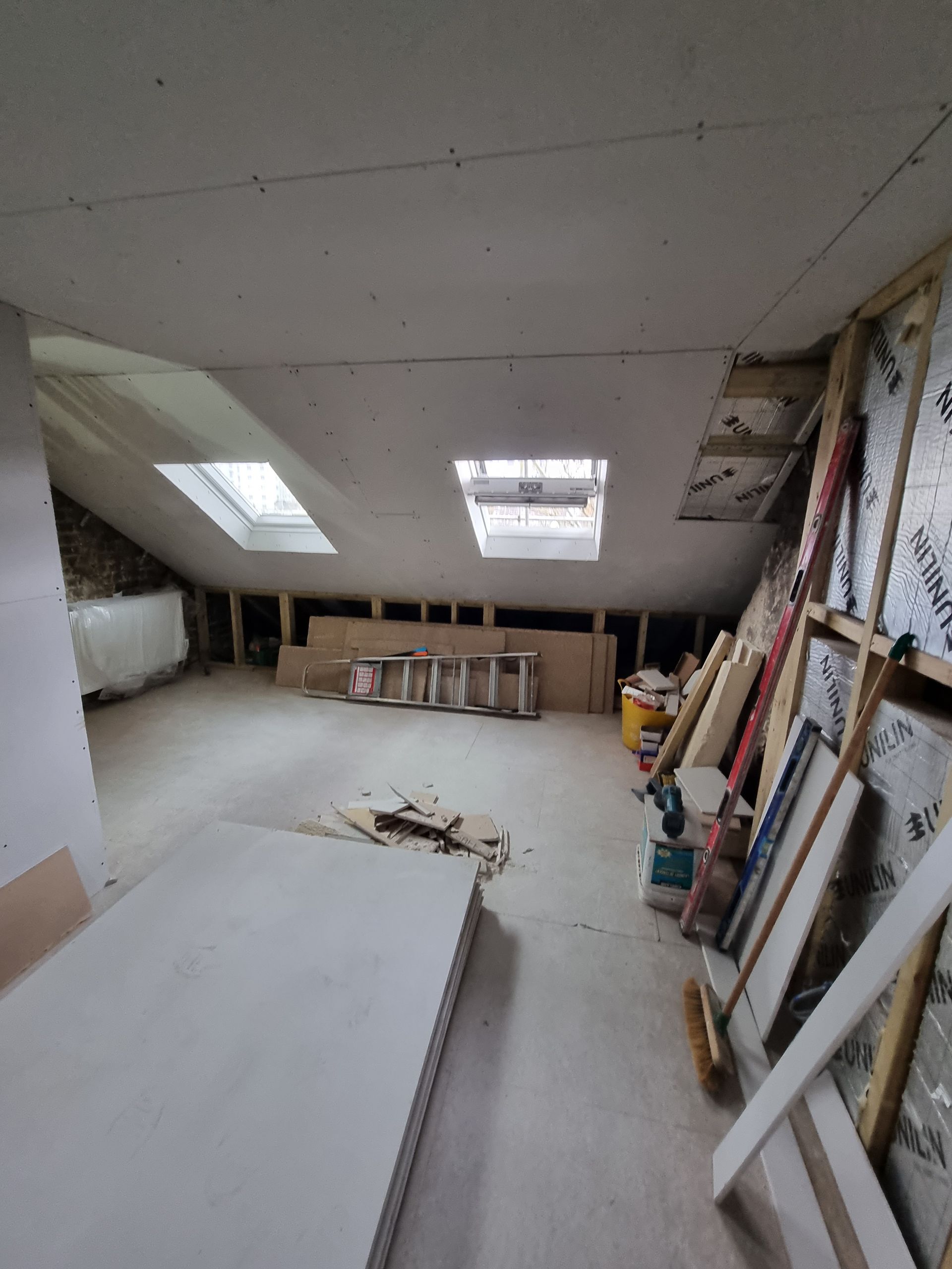 An attic with a skylight and a ladder in it.