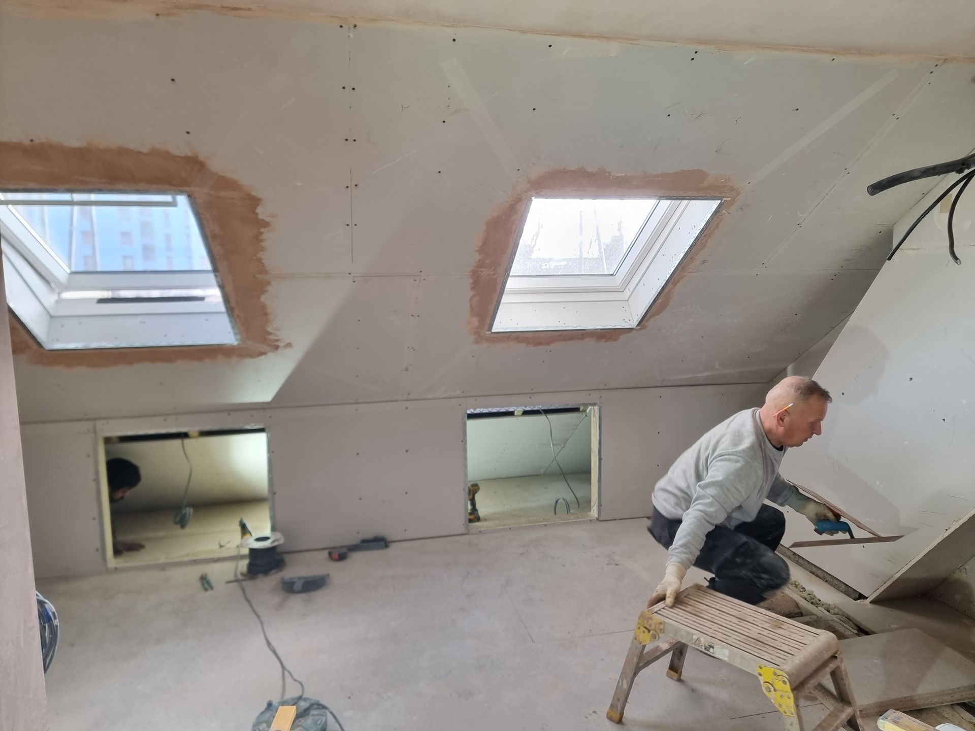 A man is kneeling on a stool in a room with skylights.