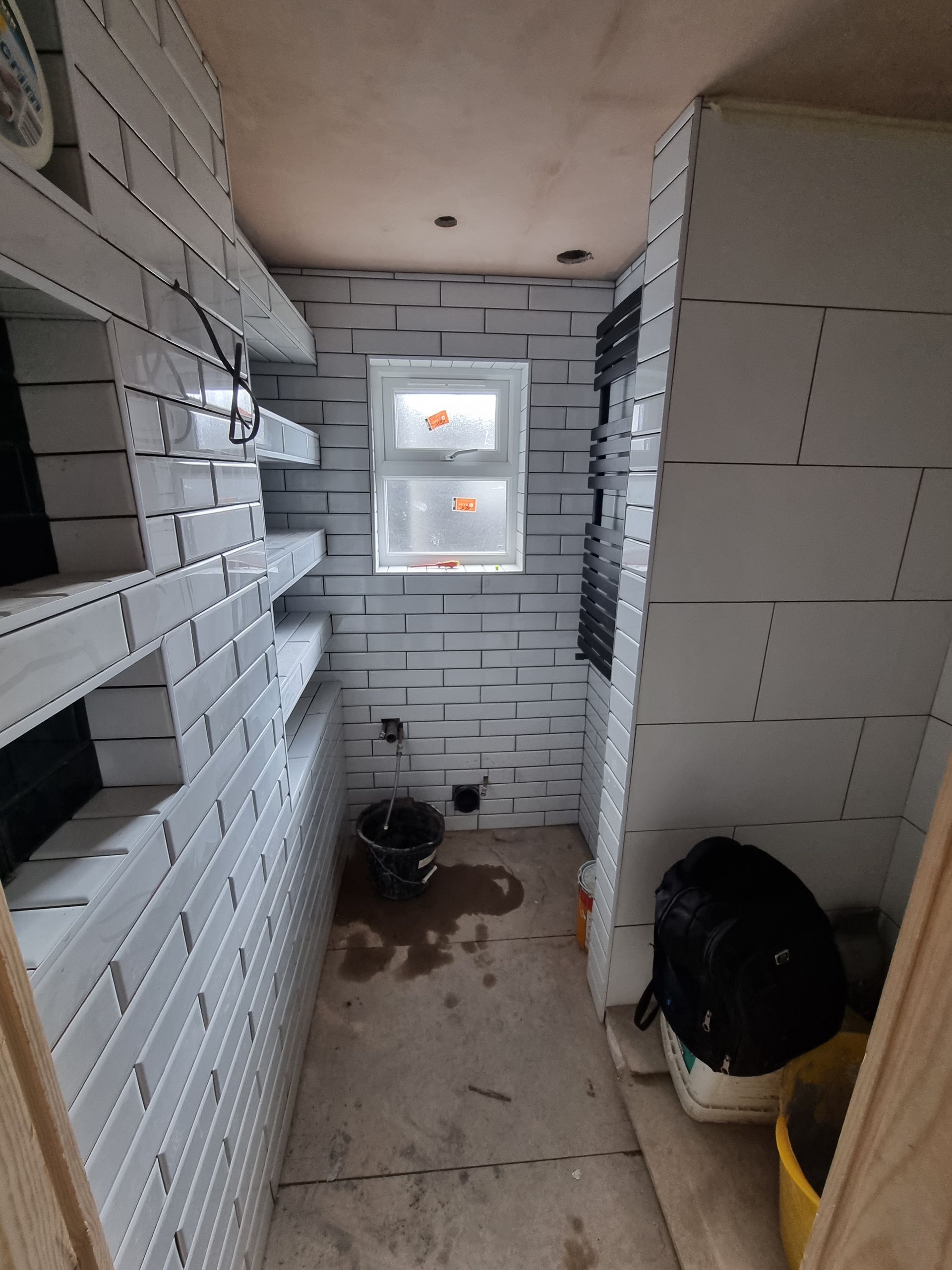 A small bathroom with white tiles and a window.