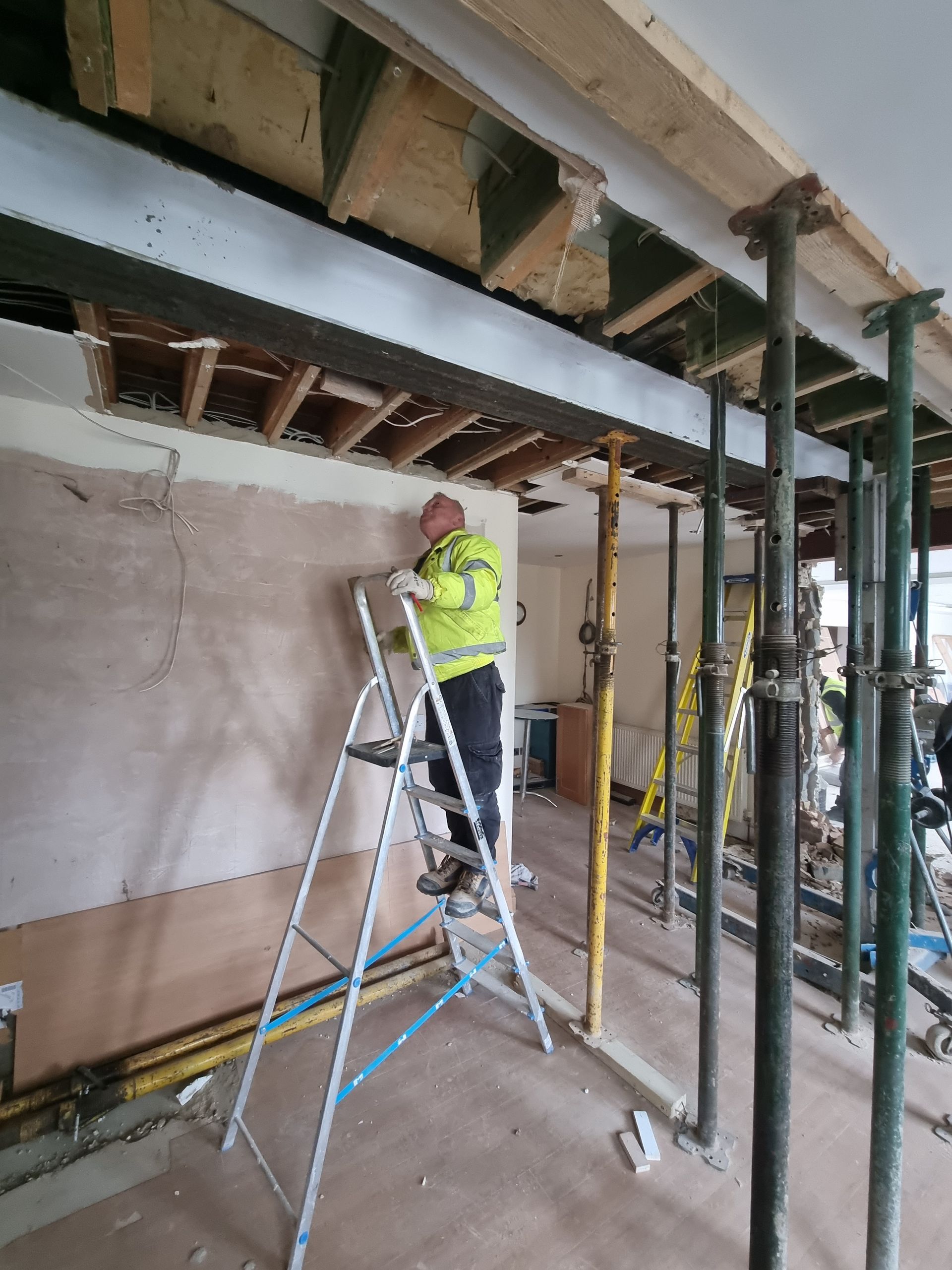 A man is standing on a ladder in a room under construction.