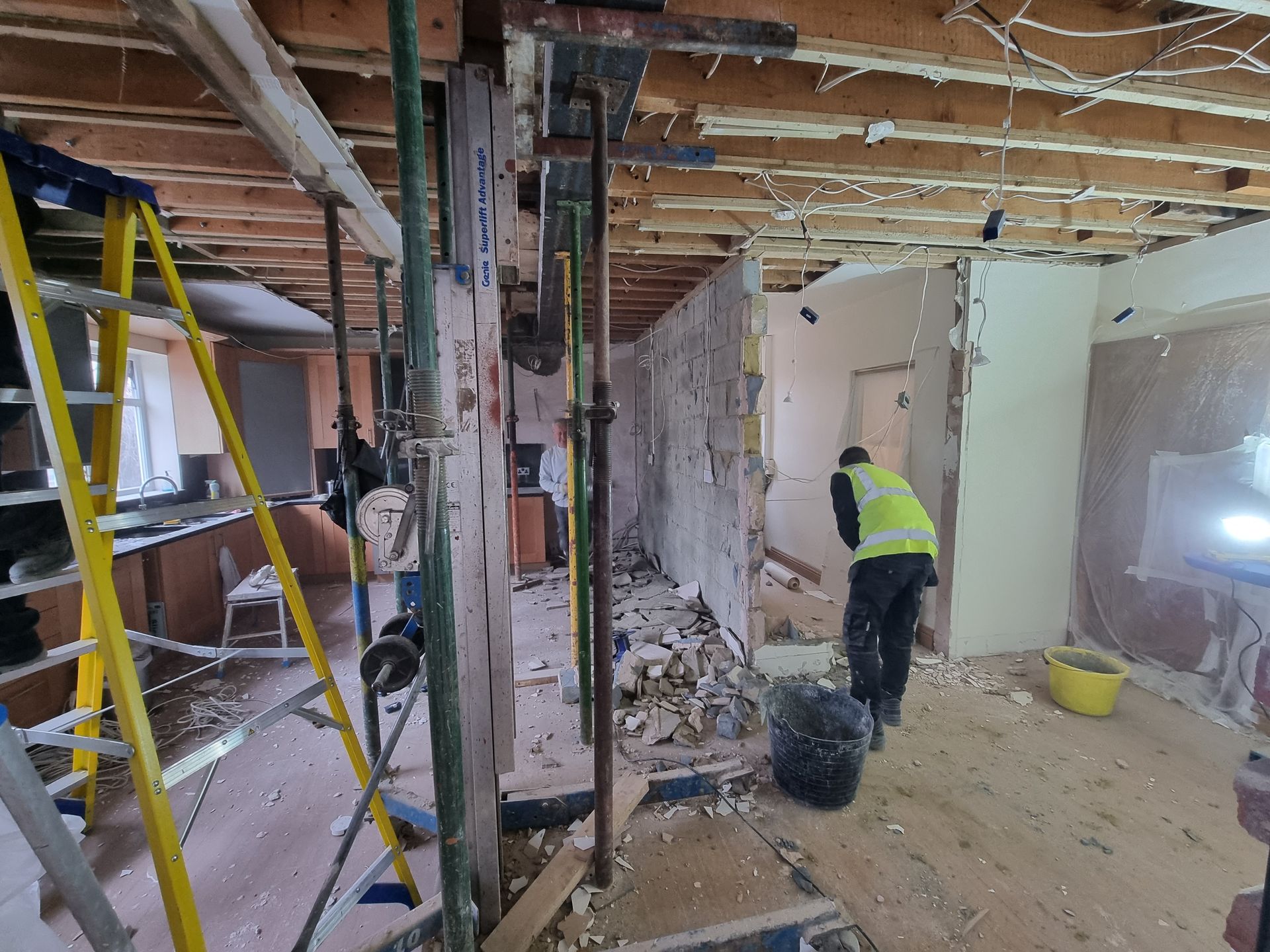 A man in a yellow vest is standing in a room under construction.