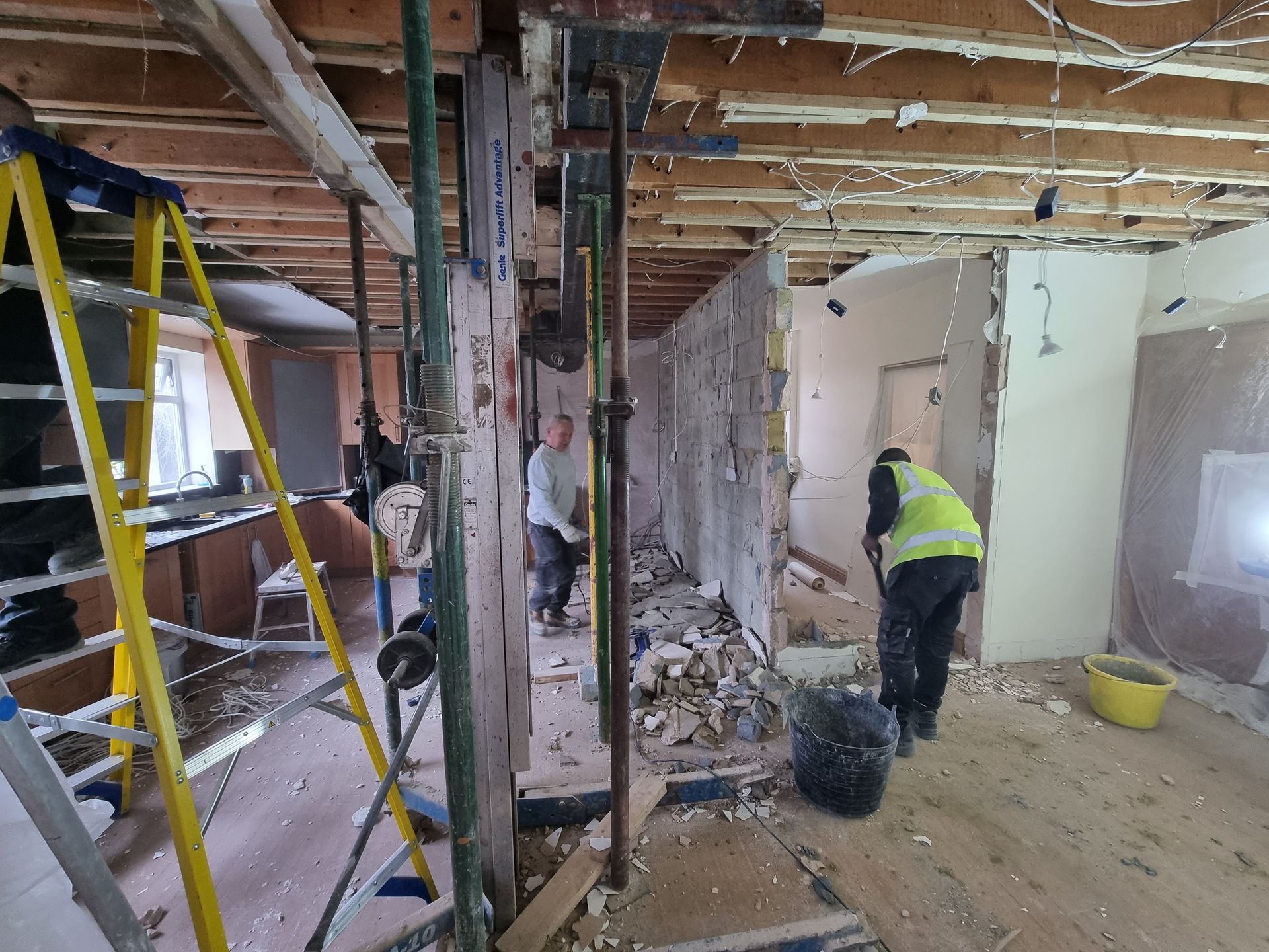 A man in a yellow vest is standing in a room under construction.