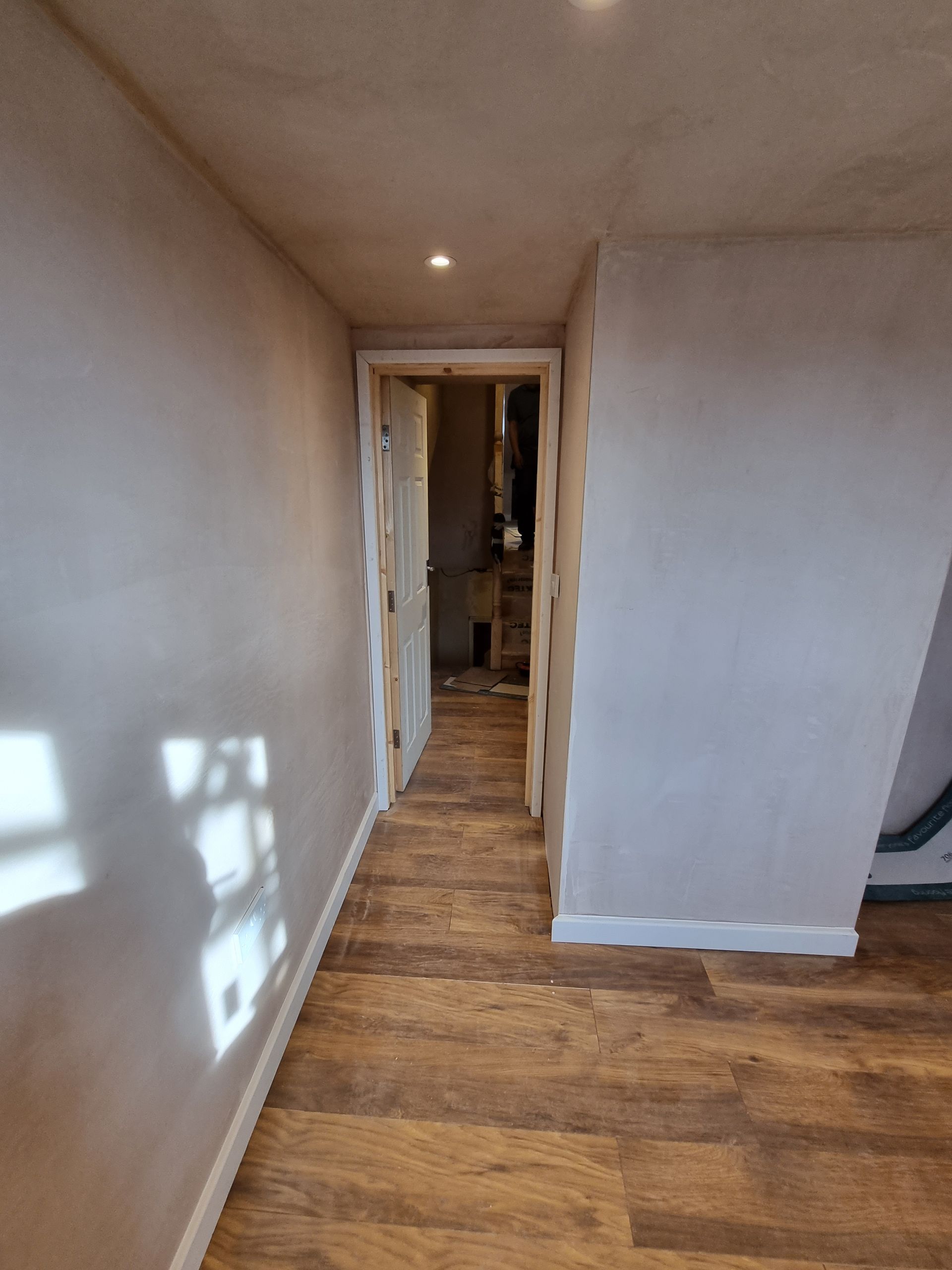 A hallway with hardwood floors and a door leading to a room.