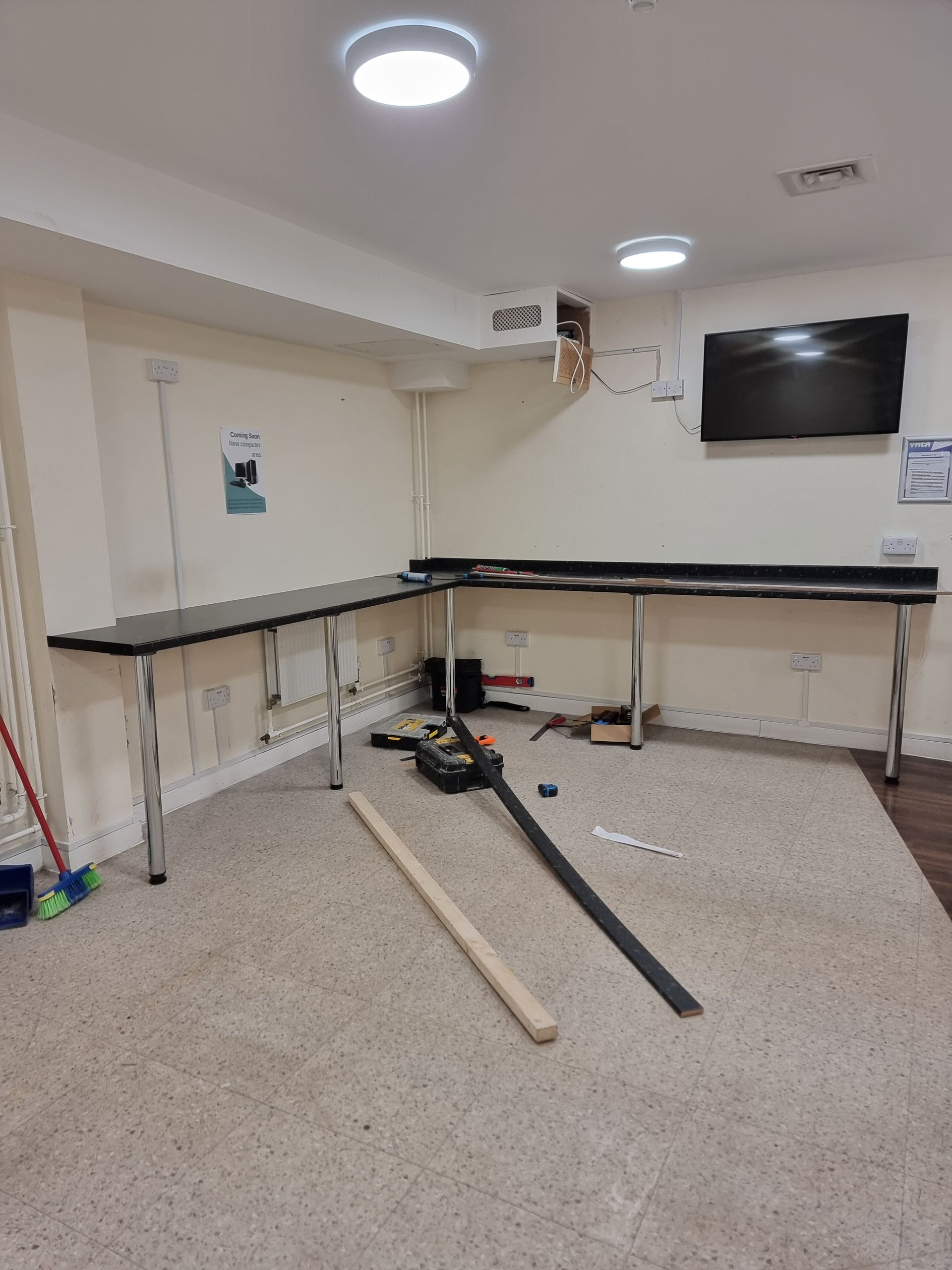 L-shaped work tables with black tops and silver legs in a room with tools on the floor.
