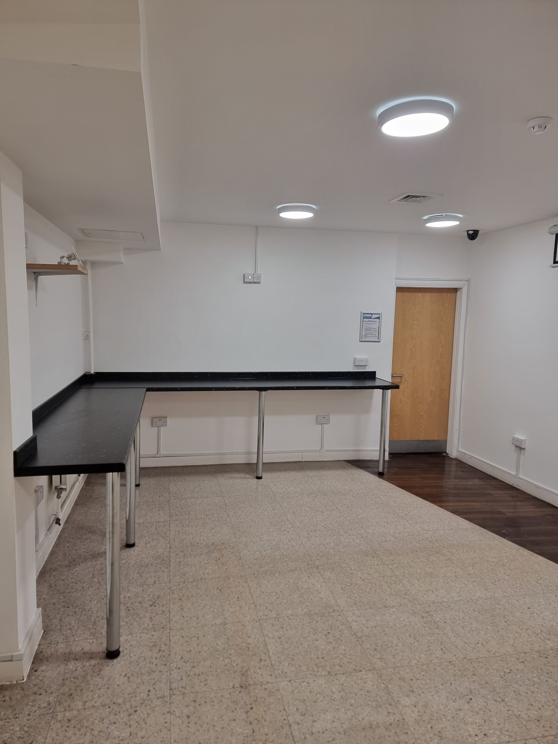 An empty room with a long counter and beige carpet. Door on the right side. White walls.