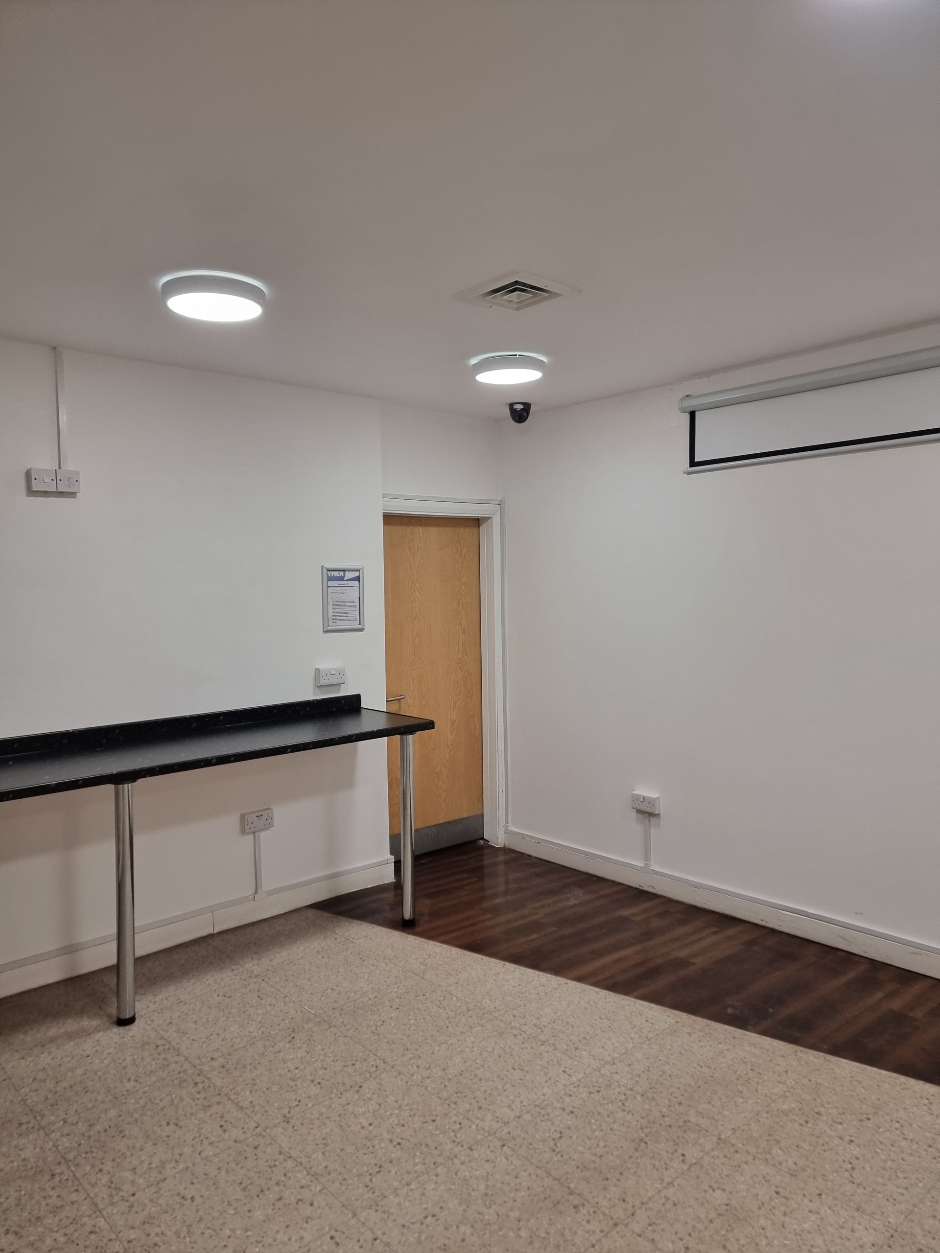 Empty room with white walls, dark floor, and a long black table.