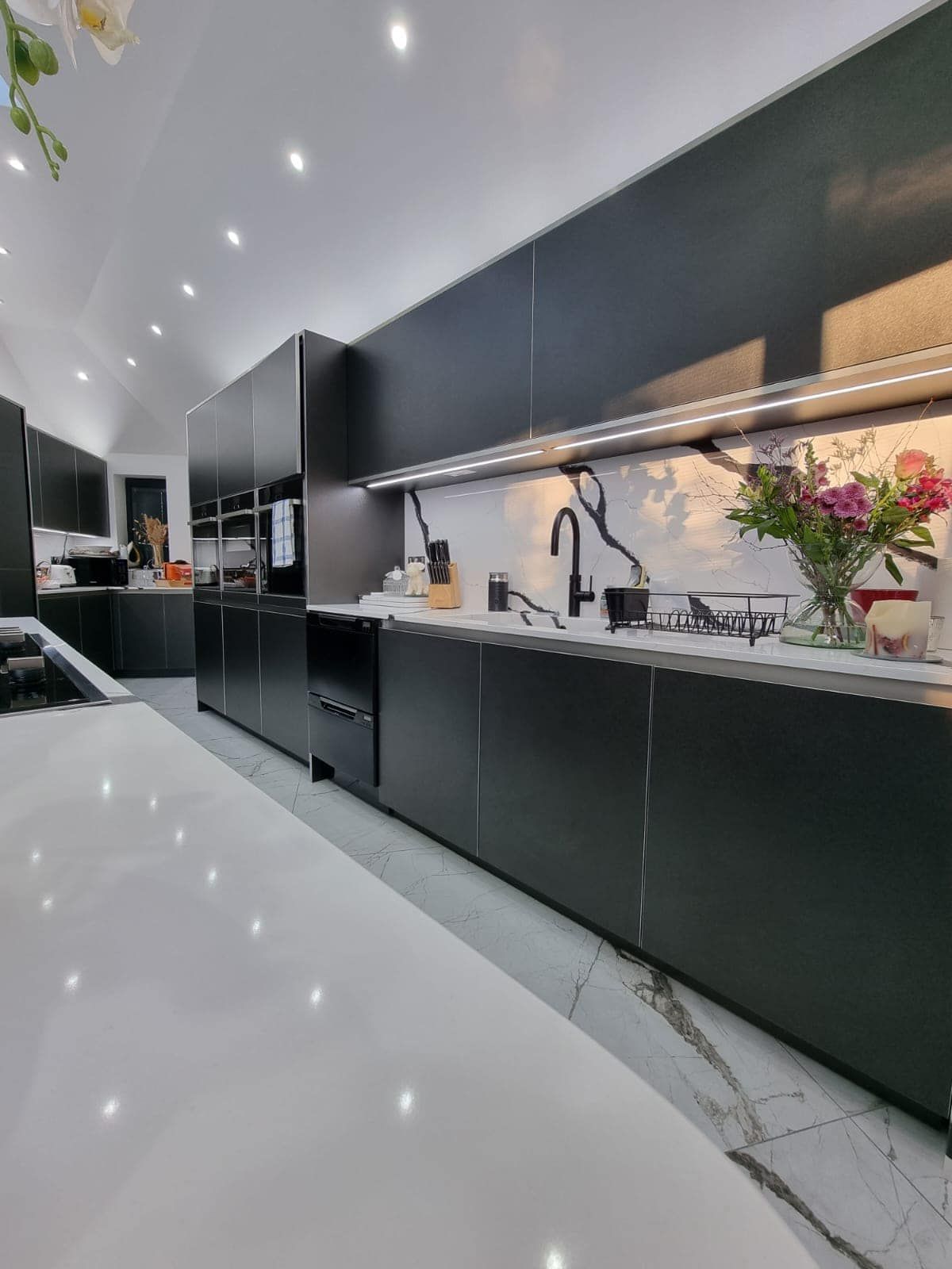 A kitchen with black cabinets and white counter tops and a vase of flowers on the counter.