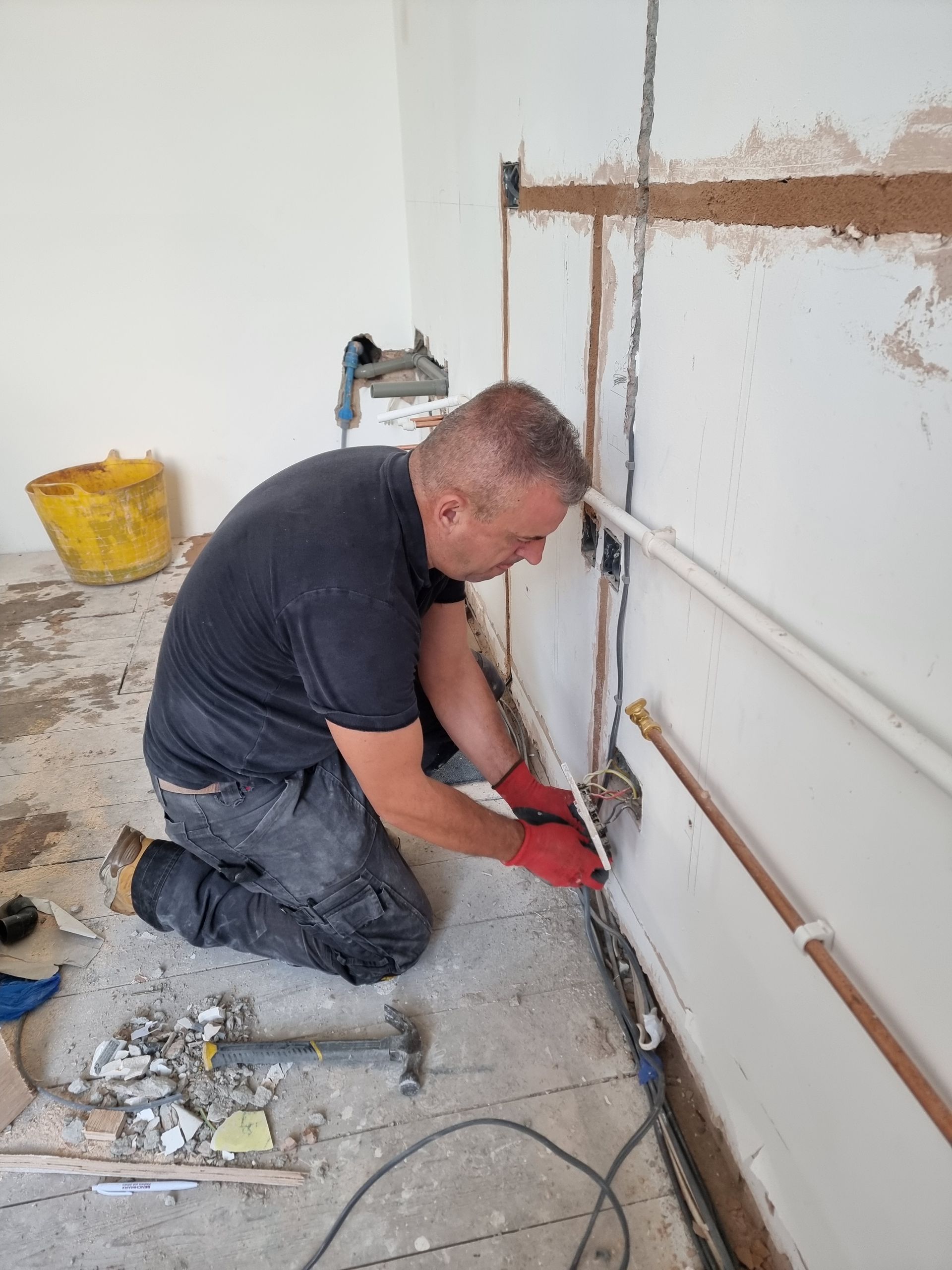 A man is kneeling down in a room working on a pipe.