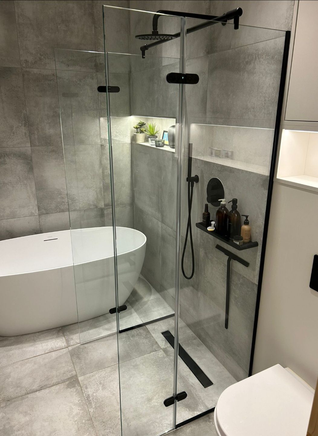 Modern bathroom with a glass shower enclosure, bathtub, and gray tile walls.