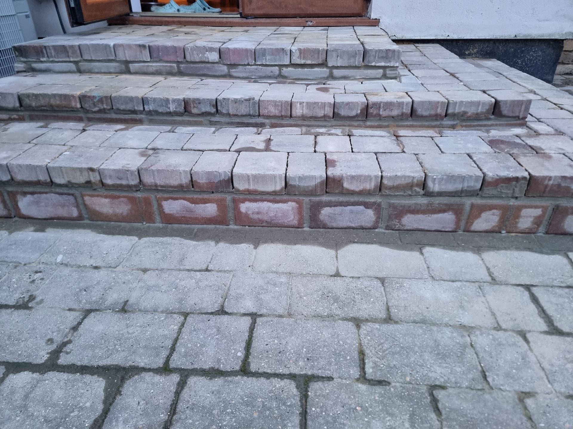 Brick steps leading to a door, with matching brick paving below. Gray and red bricks.