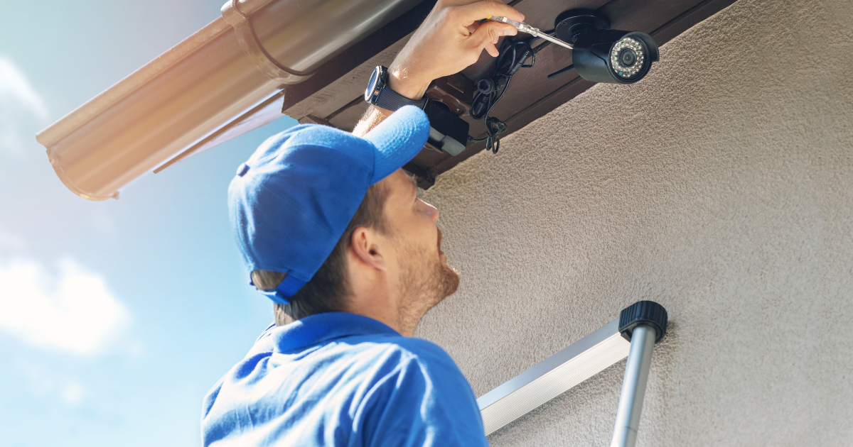 A man is installing a security camera on the side of a building.