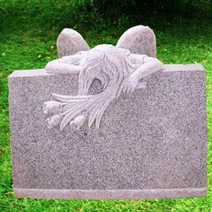 Stone grave marker with a carved grieving angel draped over the top, in a green cemetery setting
