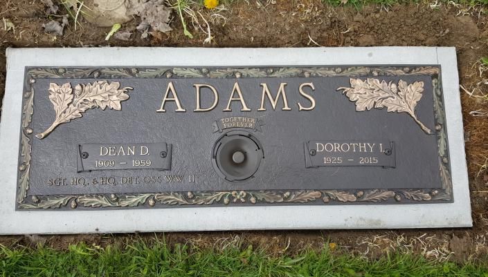 Gray stone grave marker engraved “ADAMS” with two nameplates and a small center vase.