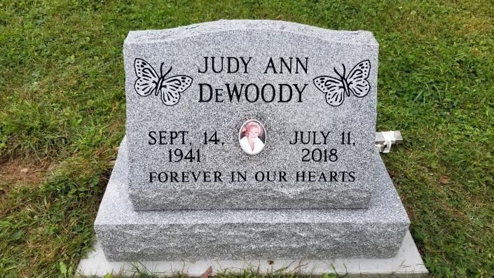 Gray granite memorial stone for Judy Ann DeWoody, with butterflies and inscription, in a grassy setting