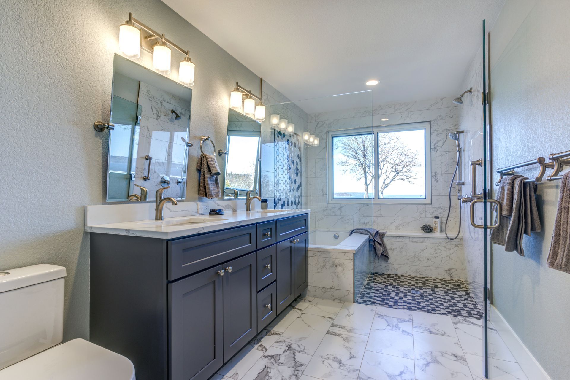 Salle de bains moderne avec sol en marbre, meuble-lavabo bleu et baignoire près d'une fenêtre.