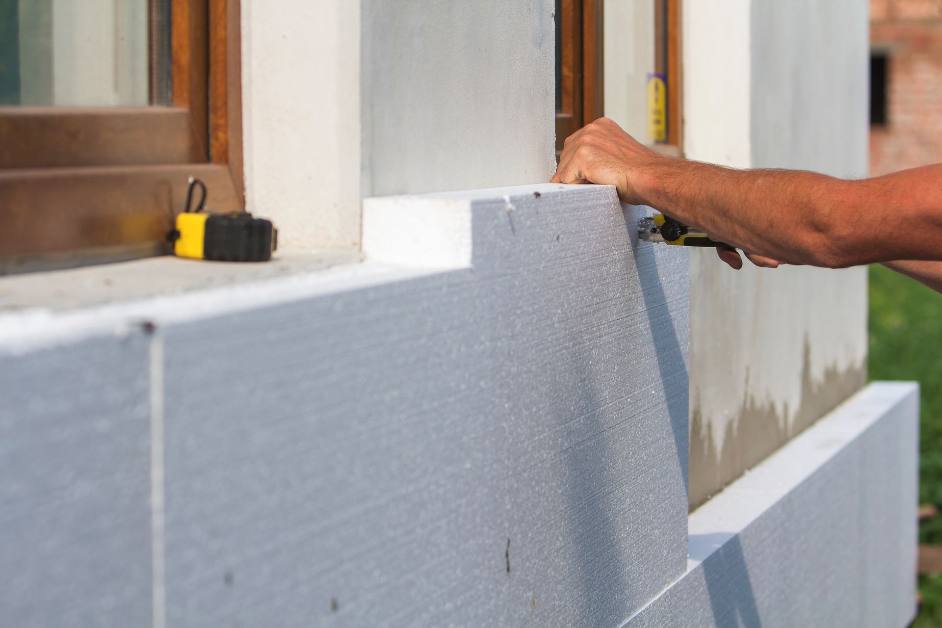 Une personne découpe de l'isolant en mousse blanche contre le mur d'un bâtiment à l'aide d'un cutter.