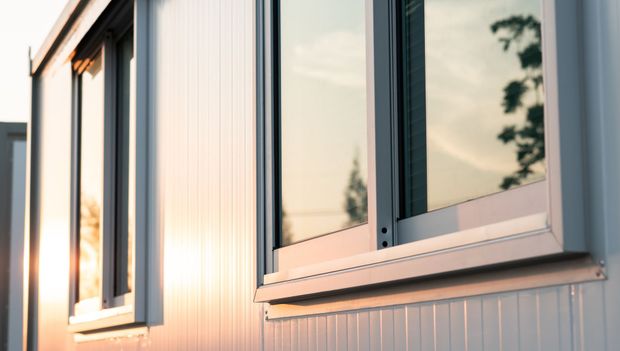 Deux fenêtres sur un immeuble blanc reflétant un coucher de soleil.