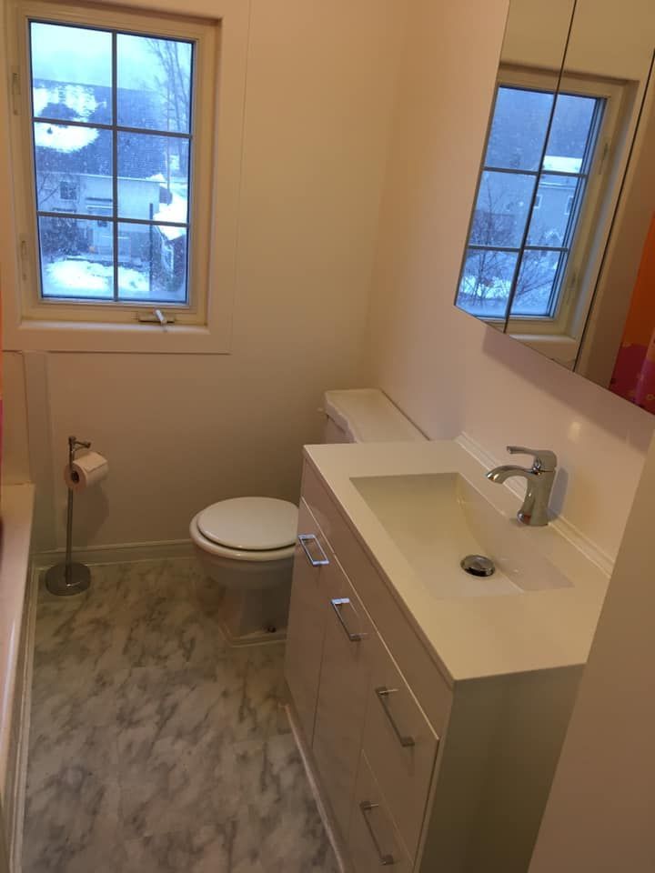 Petite salle de bains avec toilettes, lavabo et fenêtre. La pièce est claire et le sol est recouvert d'un revêtement imitation marbre.