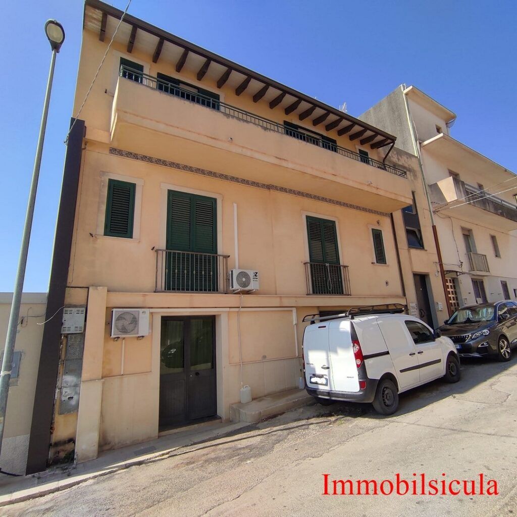 Casa a schiera beige a due piani su una strada in pendenza con furgone bianco parcheggiato e balcone.
