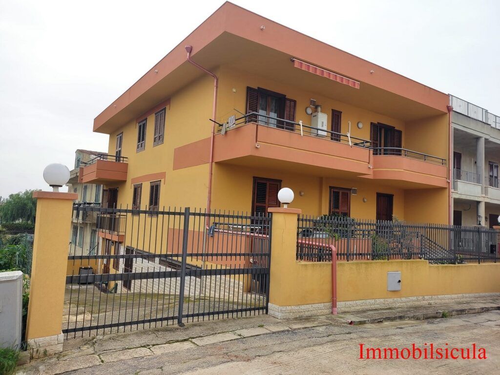 Casa arancione a due piani con cancello e balcone in una zona residenziale.