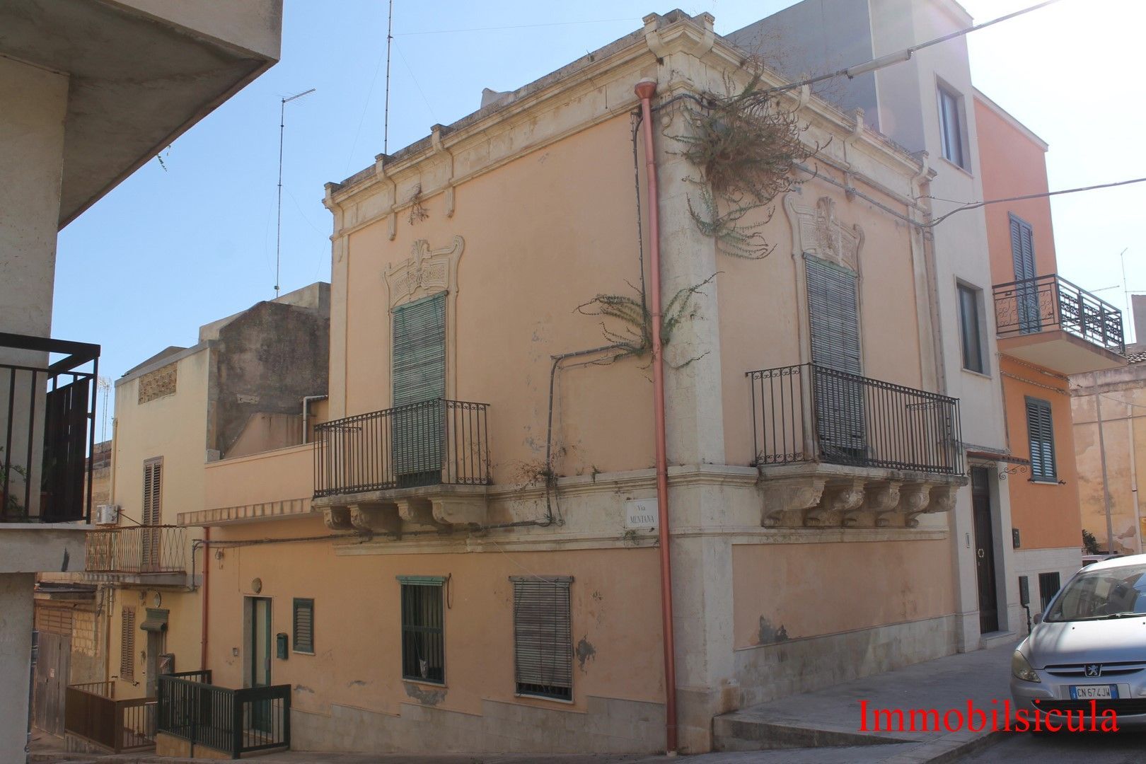 Vecchia casa d'angolo in stucco beige con balconi su una strada stretta, accanto a un edificio arancione e un'auto parcheggiata