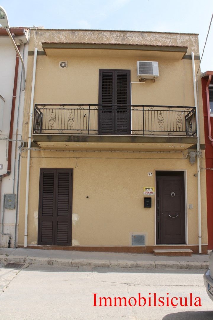 Casa beige a due piani con balcone, persiane scure e due porte d'ingresso su una strada stretta