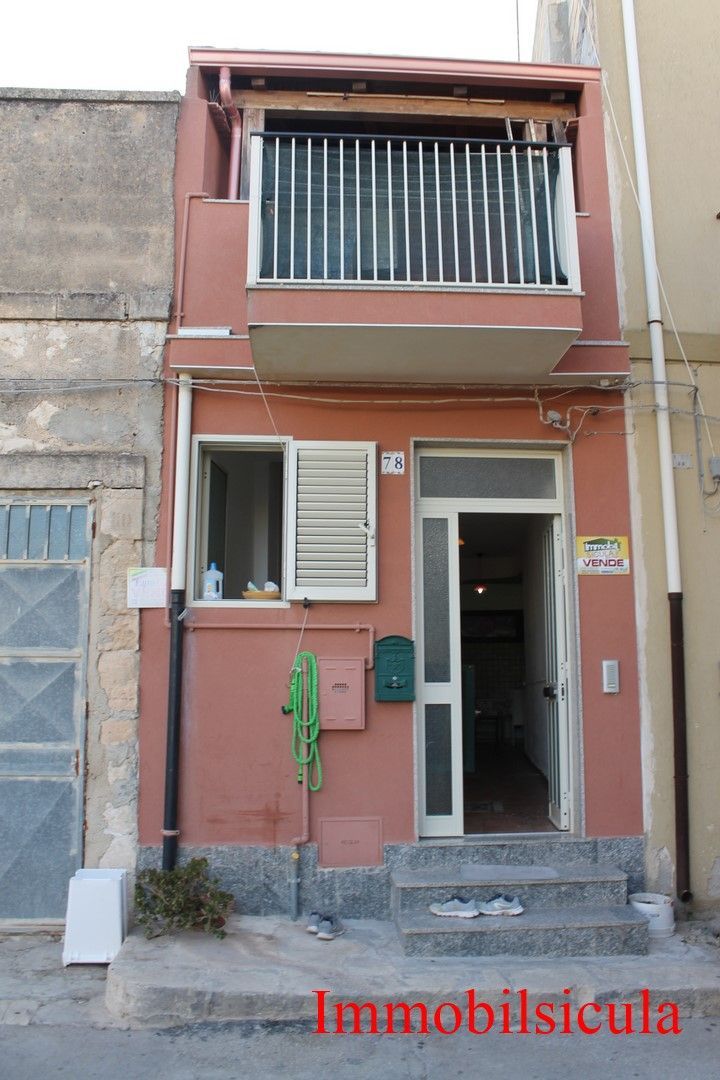Facciata stretta color pesca di una casa a schiera con balcone, persiane bianche e ingresso a livello strada.