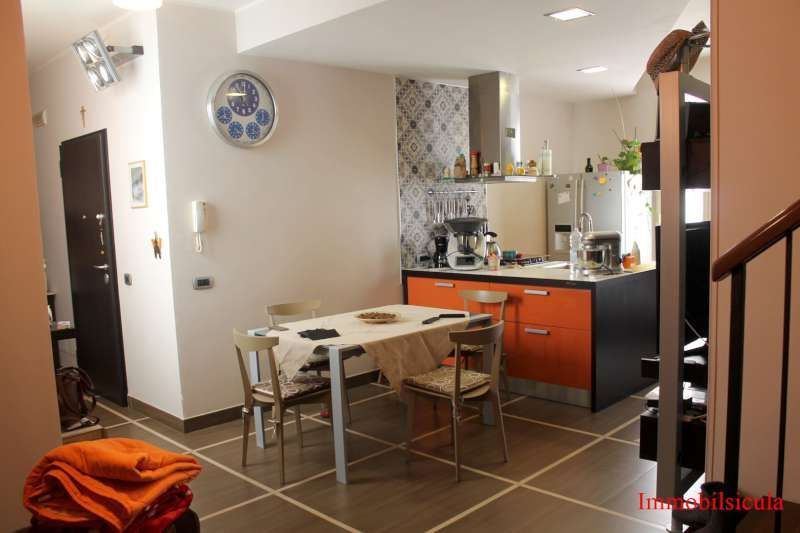Piccola cucina moderna con zona pranzo, mobili arancioni, tavolo e scala.