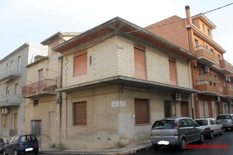 Edificio d'angolo in mattoni con finestre sbarrate e auto parcheggiate su una strada