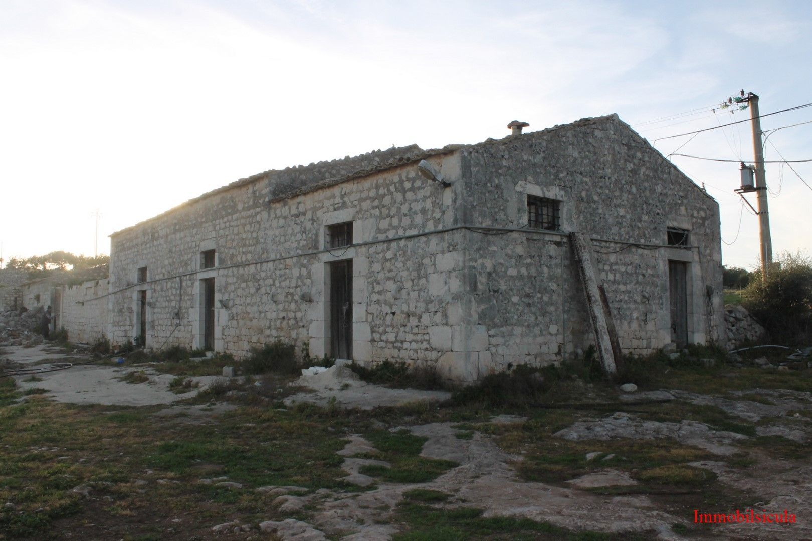 Vecchio edificio in pietra con tetto spiovente su terreno roccioso al tramonto