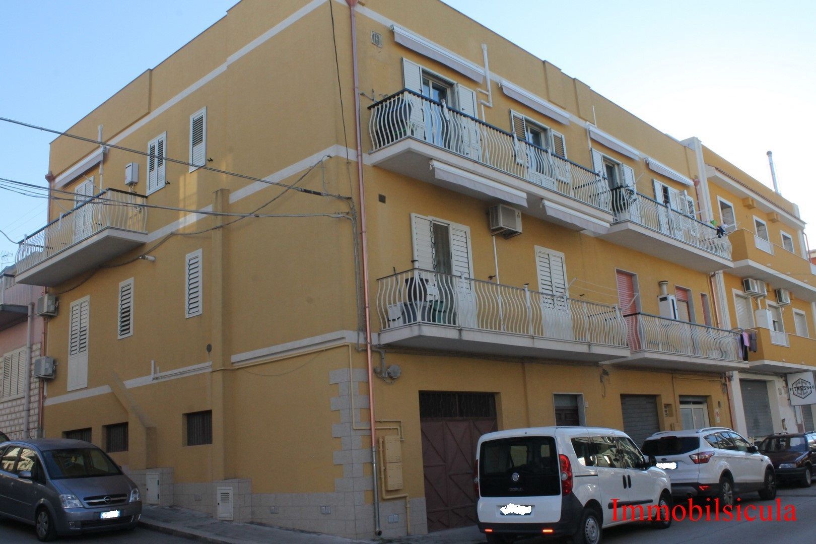Palazzo di appartamenti giallo con balconi e auto parcheggiate all'angolo della strada.