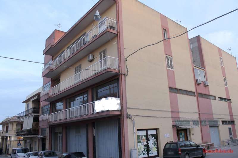 Palazzo di appartamenti rosa con balconi e auto parcheggiate all'angolo della strada.