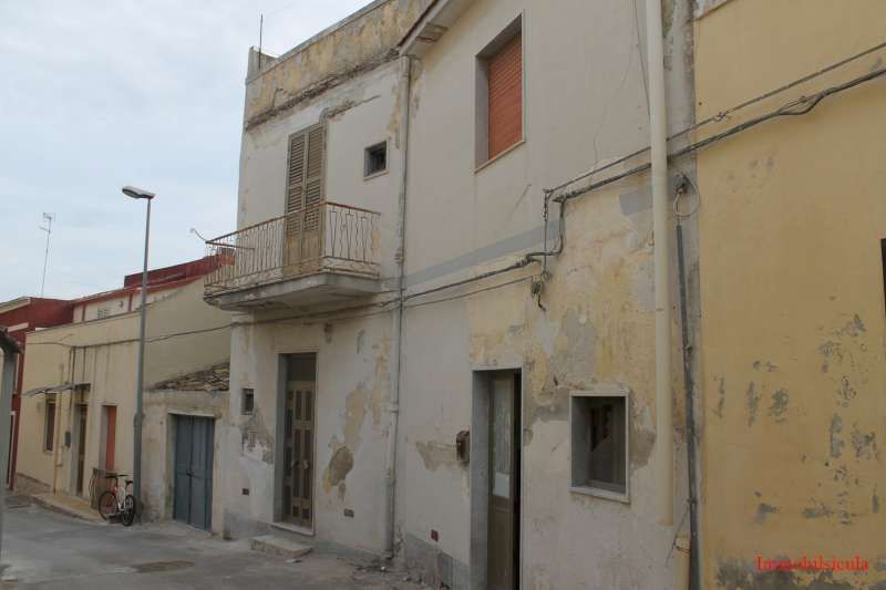 Palazzi residenziali color beige, consumati dal tempo, che si affacciano su una strada stretta, con balconi e finestre con persiane.