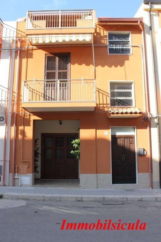 Casa a schiera arancione a tre piani con balconi e finestre con persiane, affacciata su una strada, con un'insegna "Inmobsicula" in basso.