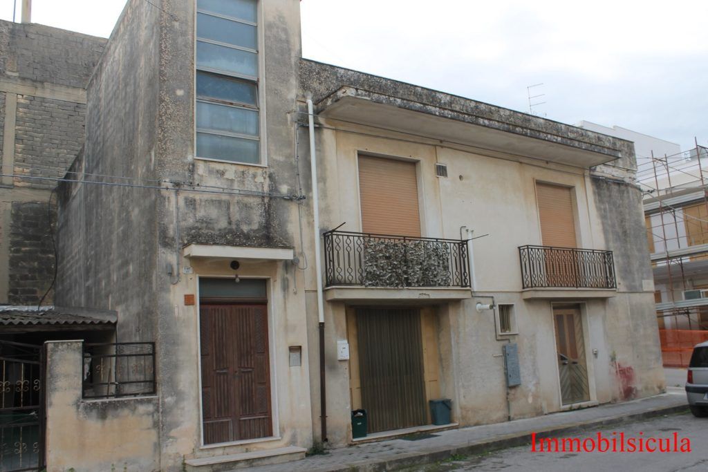 Vecchio edificio in pietra consumato dal tempo con finestre sbarrate e piccoli balconi in una strada tranquilla.