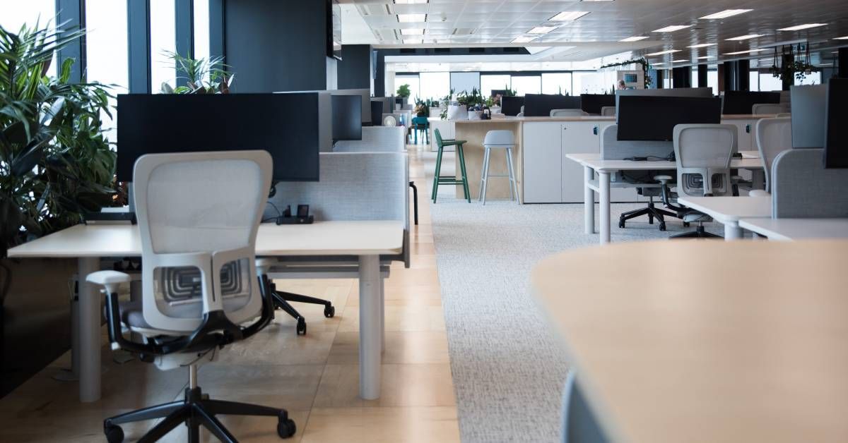 A large corporate office space with various individual and collaborative desk setups with computers and chairs.