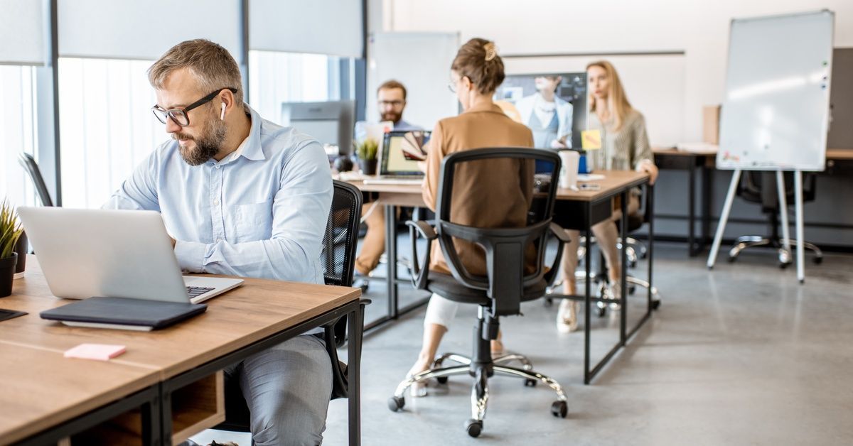 Several business professionals sitting at various desks with chairs and laptops, working in a co-working office space.