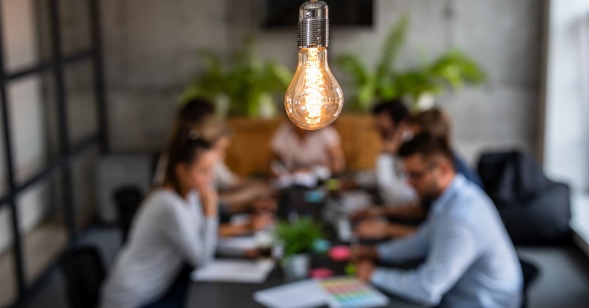 In the background is a table full of people who are all blurry. In the foreground is a lightbulb.