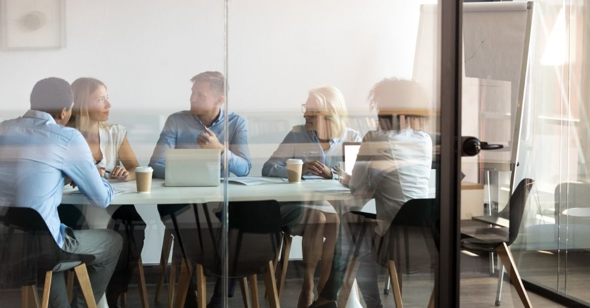 There is a group of people, all sitting around a conference table. There is a poster set up next to the table.