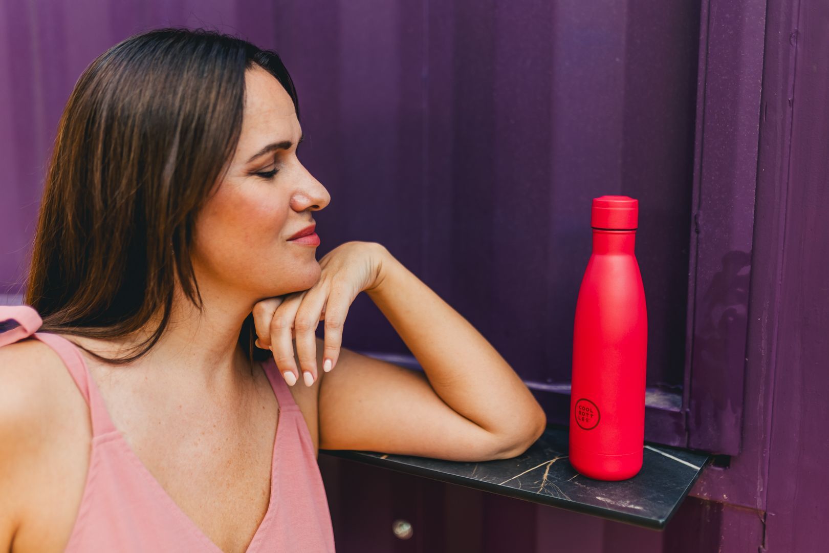 Mulher sentada a olhar para uma garrafa de água térmica vermelha da Cool Bottles