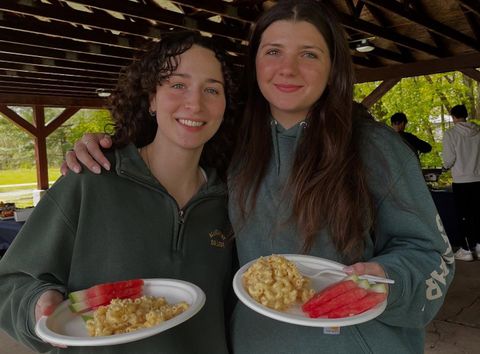 Two smiling people standing in an outdoor pavilion, each holding a plate.