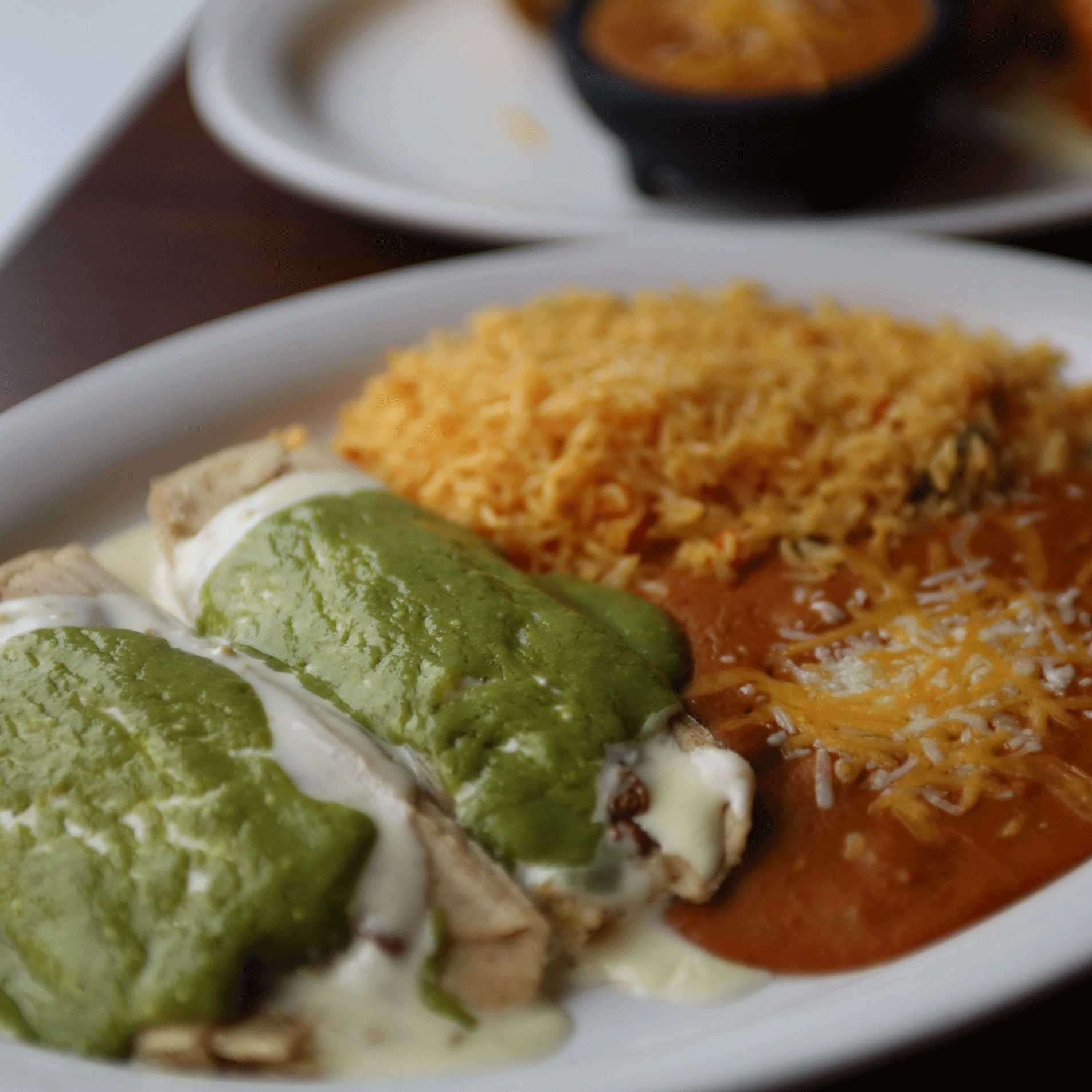 Enchiladas covered in green sauce and white cheese, served with rice and refried beans.